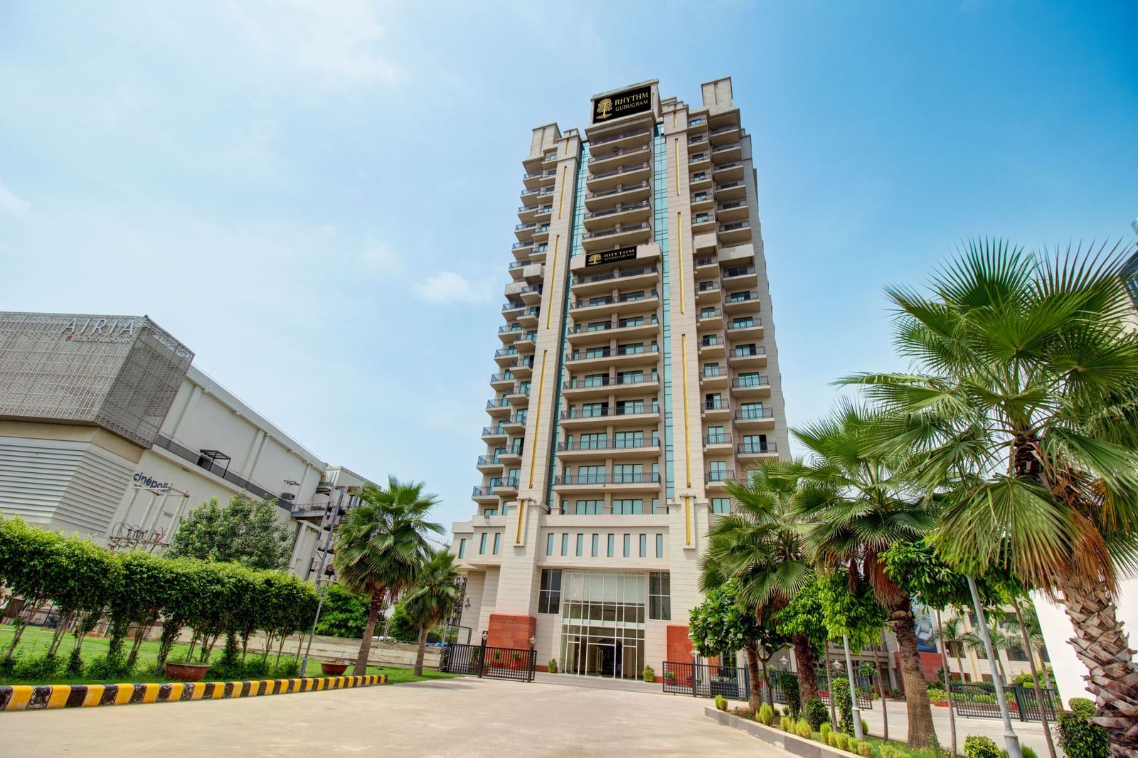 Facade view of the Entrance to Rhythm Gurugram with trees and paved road leading to the hotel