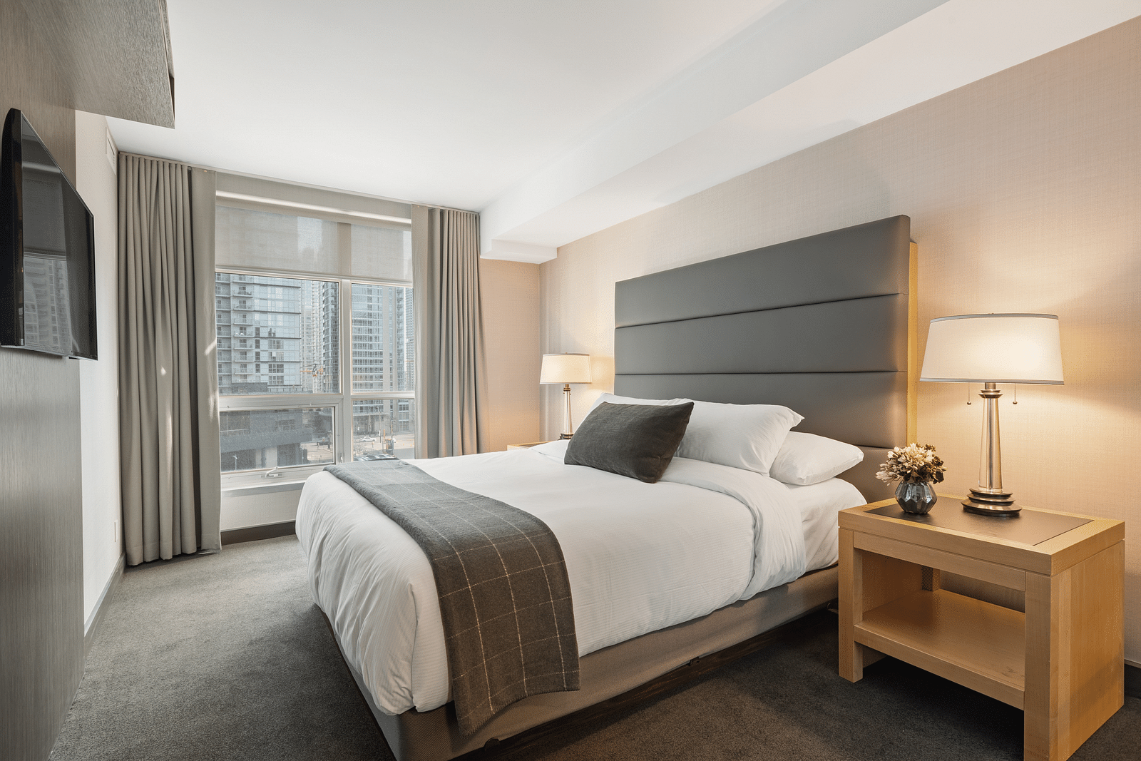 A double bed with cushioned headboard and a side table with a lamp on it at Rhythm Gurugram