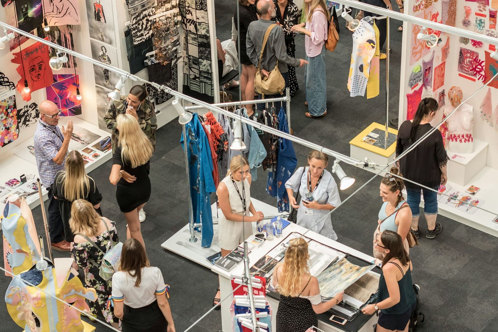 A top view of an exhibition with many stalls and people interacting with one another.