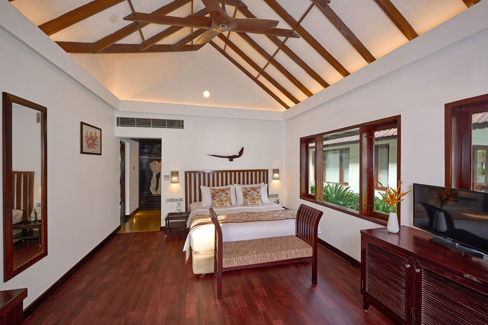 an overview of a room of with a bed, a side drawer, a TV and a full length mirror - Rhythm Kumarakom.