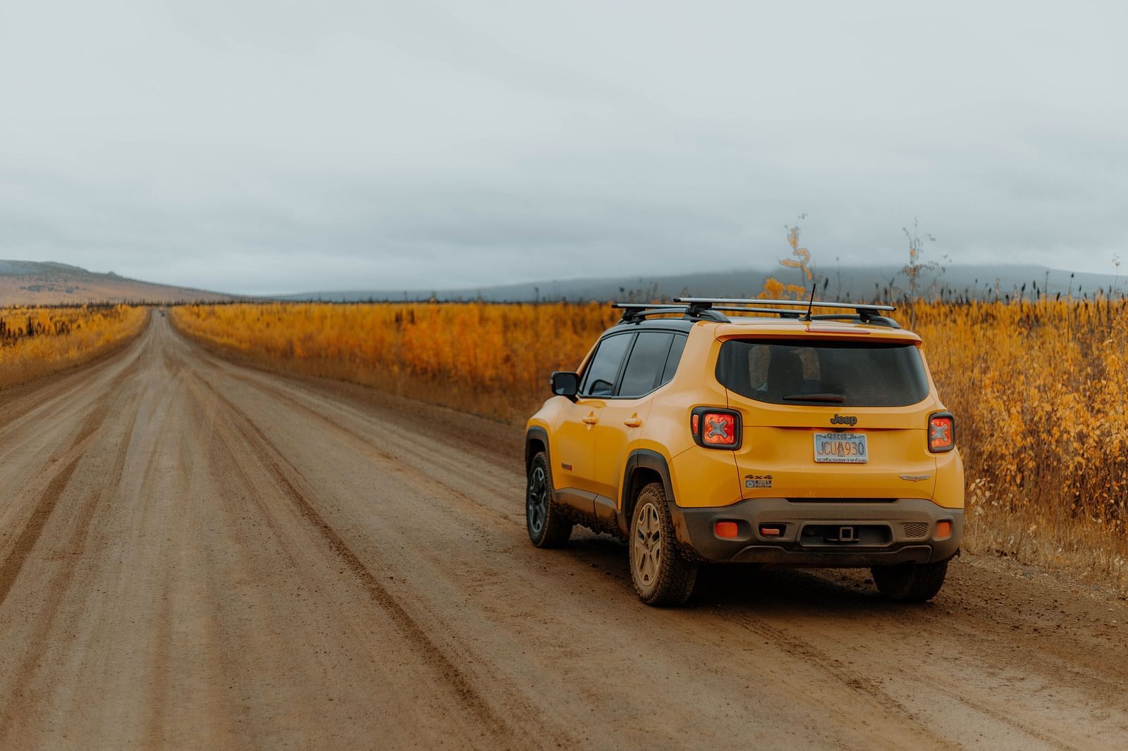 an image of solitary car travelling on a straight road with dried grass on either side.