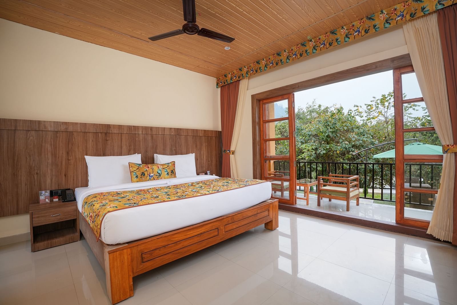 Bungalow featuring a spacious bed with wooden headboards, bedside table, and a large balcony at Summit Green Lake Tea Resort & Spa, Kaziranga
