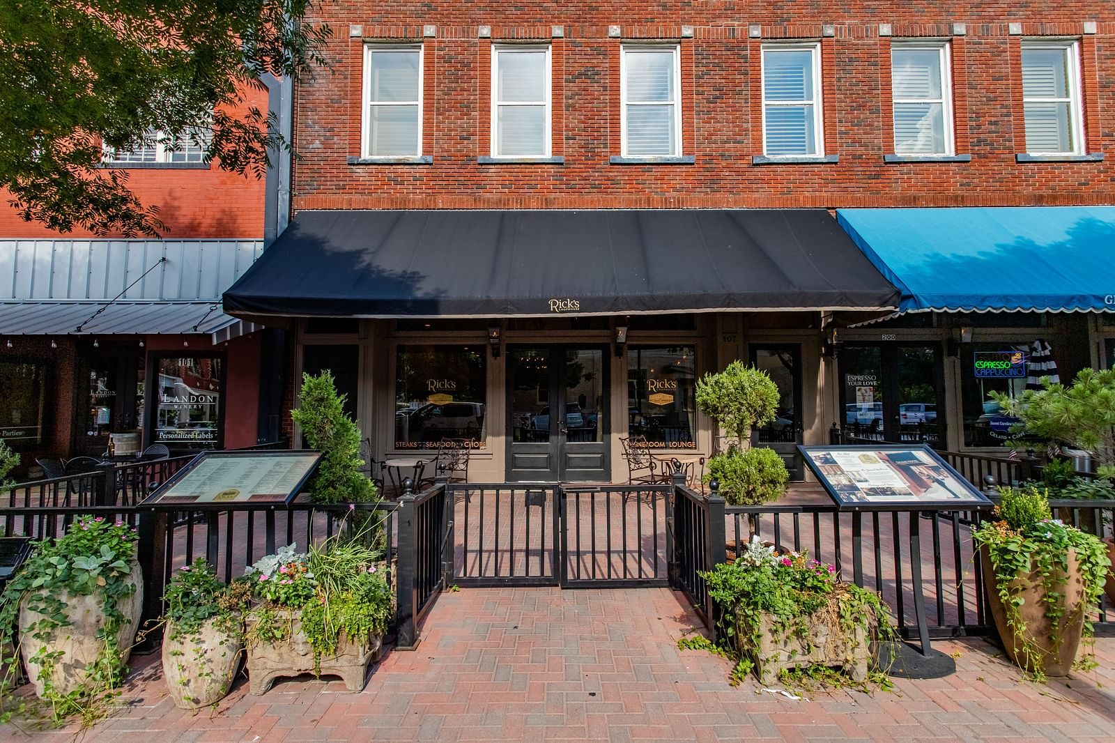 A view of a restaurant entrance with a gated patio, decorative plants, and a canopy above the doorway.- The Grand Hotel & Ballroom, McKinney