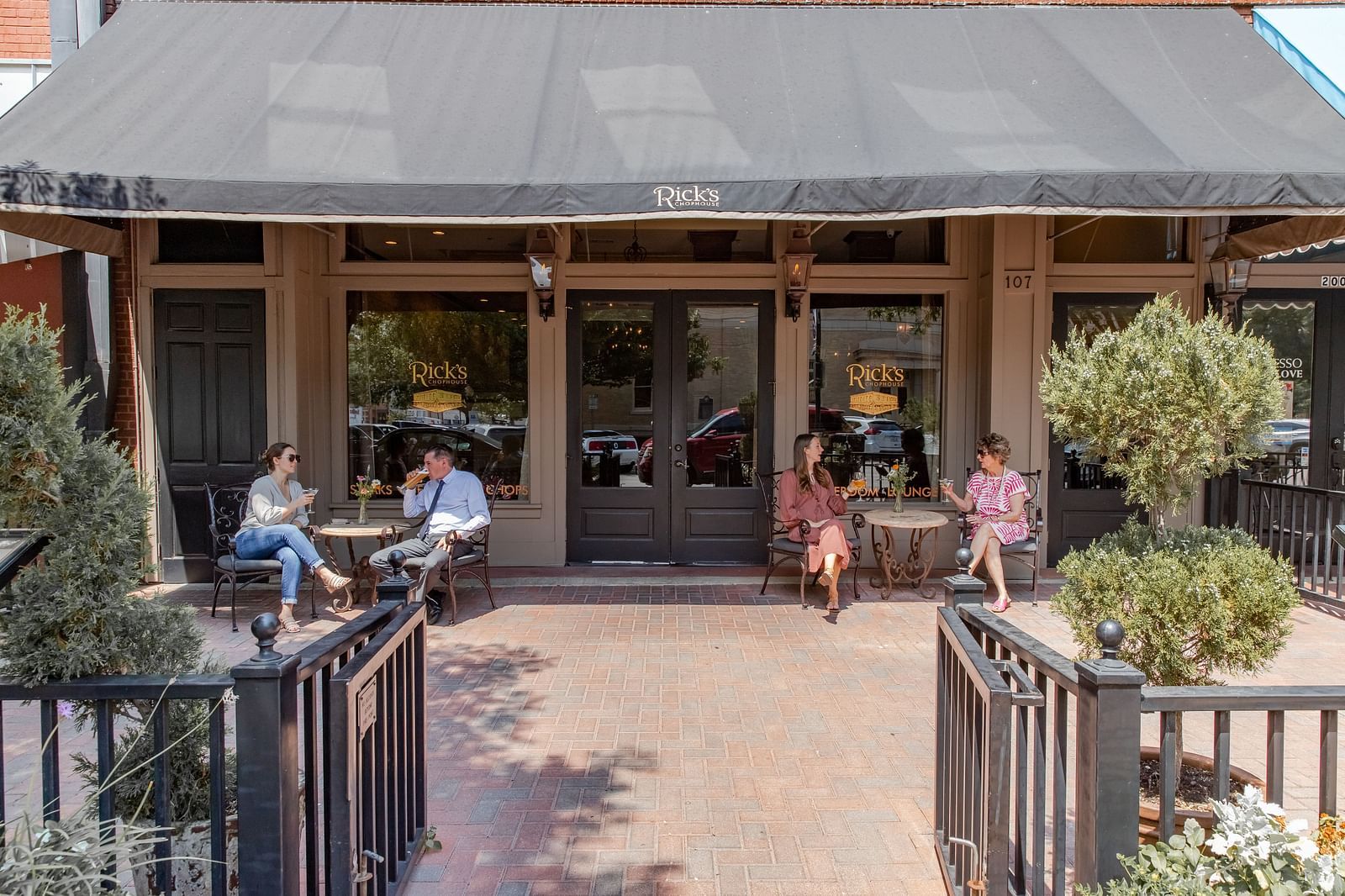 A restaurant entrance with a ramp and double doors, with people sitting near the outdoor seating area.- The Grand Hotel & Ballroom, McKinney