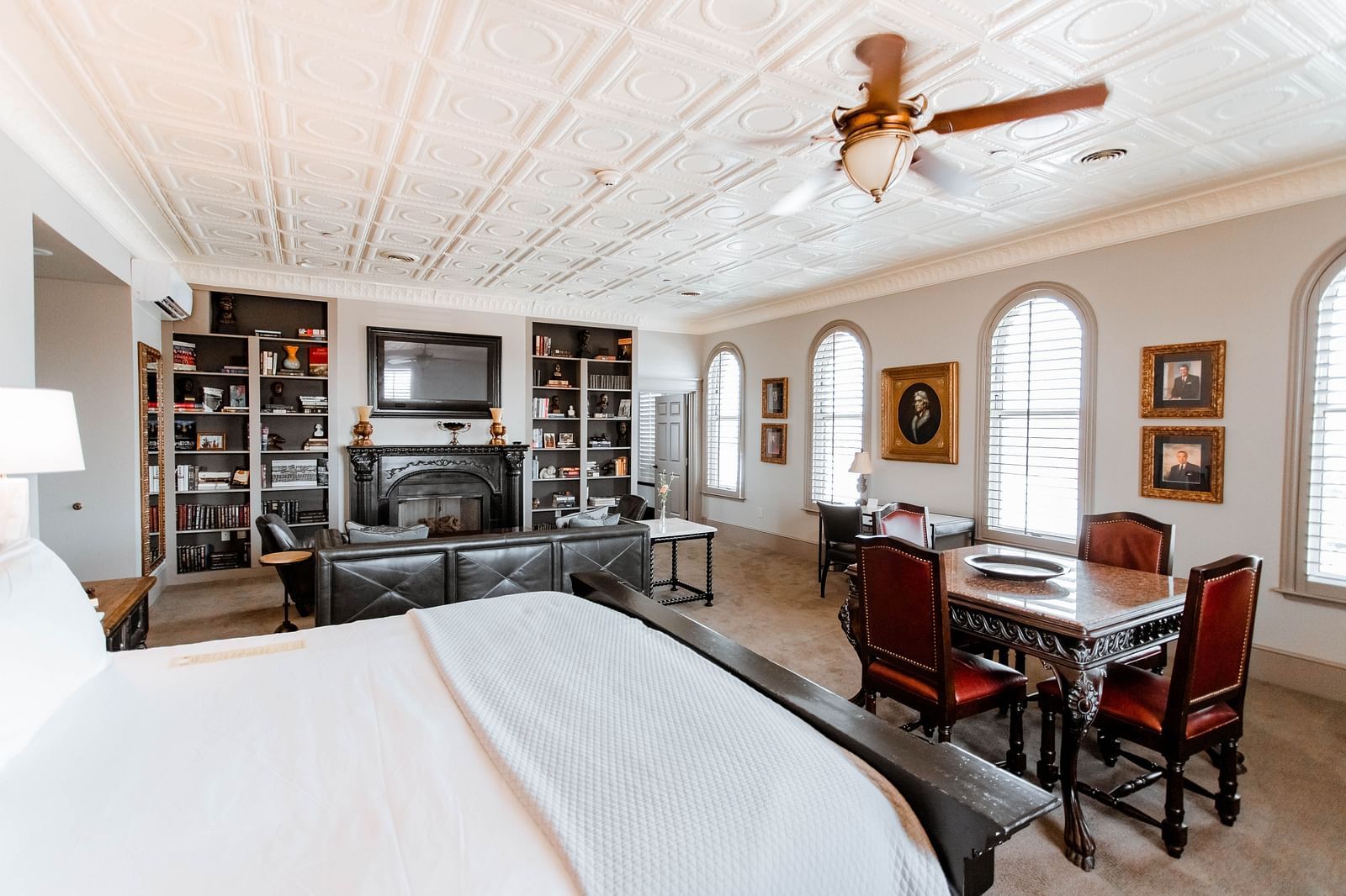A large bedroom featuring a bookshelf with books, a cosy seating area, and a comfortable bed, providing a relaxing environment - The Grand Hotel & Ballroom, McKinney