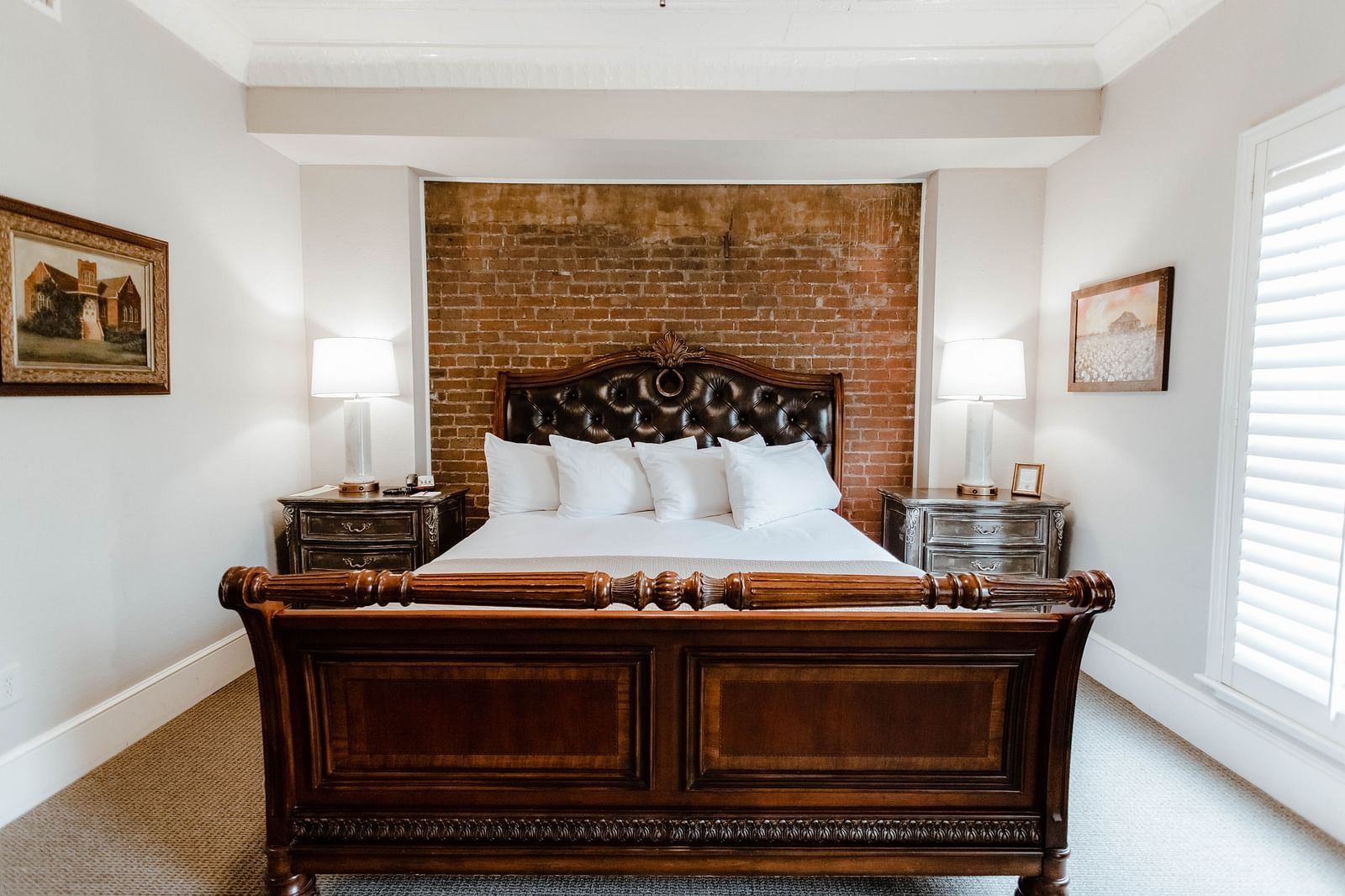  A classic bedroom with dark wood furniture, a large bed, and soft, natural lighting from the window, providing a serene retreat - The Grand Hotel & Ballroom, McKinney