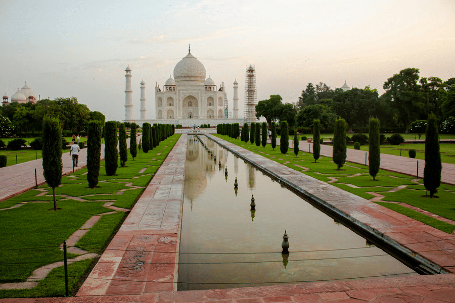 A scenic view of Taj Mahal in Agra, India featuring a long pathway and trees on either side of the small pool