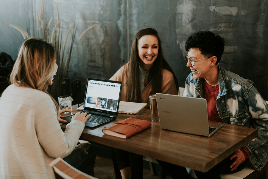 Three people sitting around a table laughing and working together on laptops at a cafe