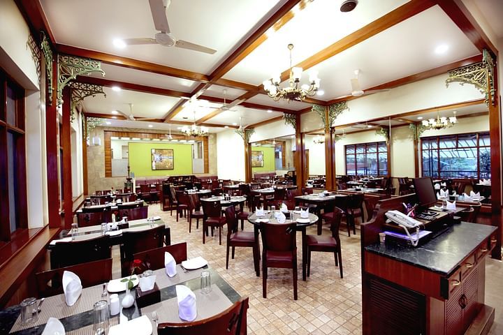 Interiors of Rani Rasoi at Zaras Restaurant with neatly arranged tables and chairs, elegant chandeliers, wooden accents, and large windows overlooking the outdoor scenery.