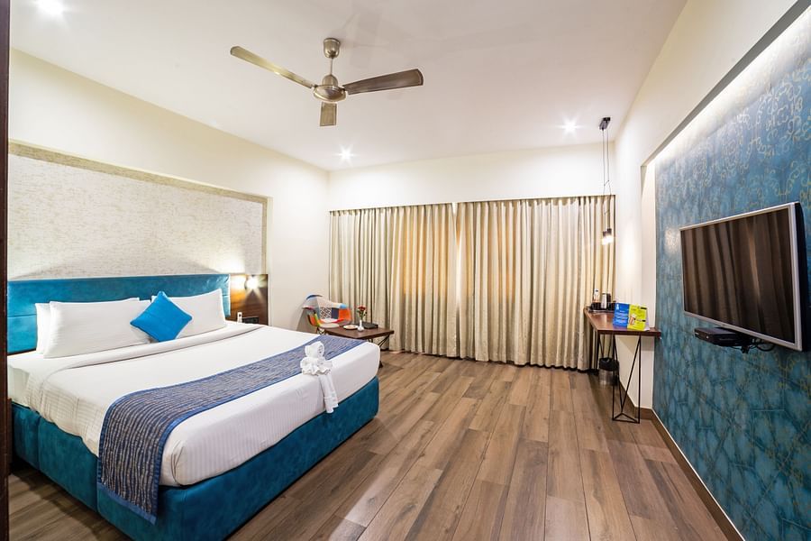 A corner view of the spacious and well-lit hotel room at Icon Boutique Hotel by Bhagini, Domlur, with a bed, a flat-screen TV, and a seating area. with sofa