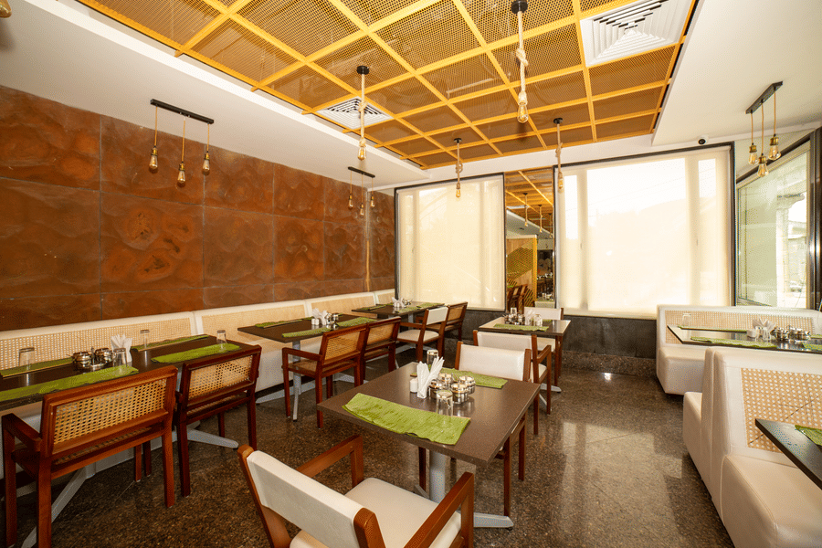 A detailed view of a section with dining tables and chairs featuring green placemats next to a brown wall at Icon Express By Bhagini, Mahadevapura.