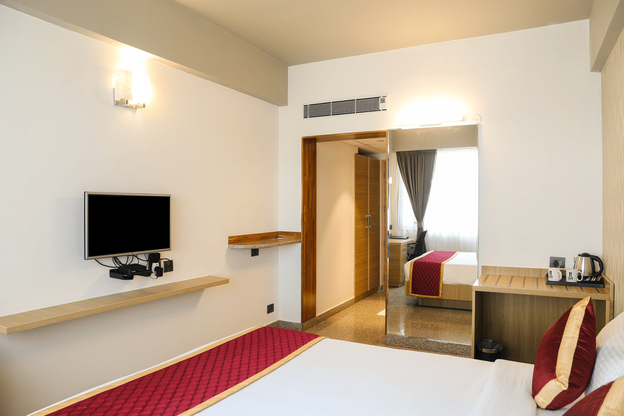 A double bed, a wall-mounted television, and a large mirror at Icon Express By Bhagini, Mahadevapura.