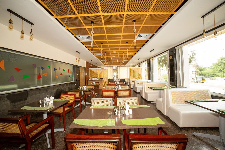 Interior of the restaurant dining room, featuring multiple tables and chairs under a patterned wooden ceiling at Icon Express By Bhagini, Mahadevapura.