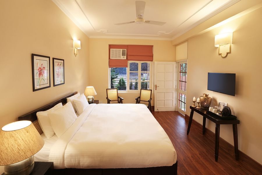 An image of a Super Deluxe Room equipped with soft bedding, modern furniture, flat TV screen, and a seating area with chairs  - Lamrin Boutique Cottages Rishikesh