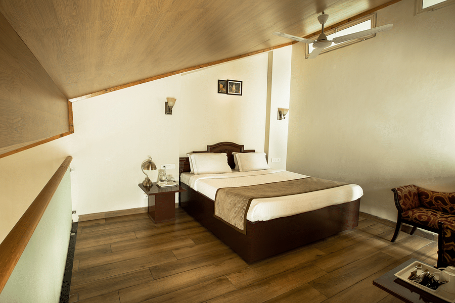 A cosy room with a queen size bed with wooden ceiling and pristine white bedsheets along with room amenities - Lamrin Norwood Green, Palampur