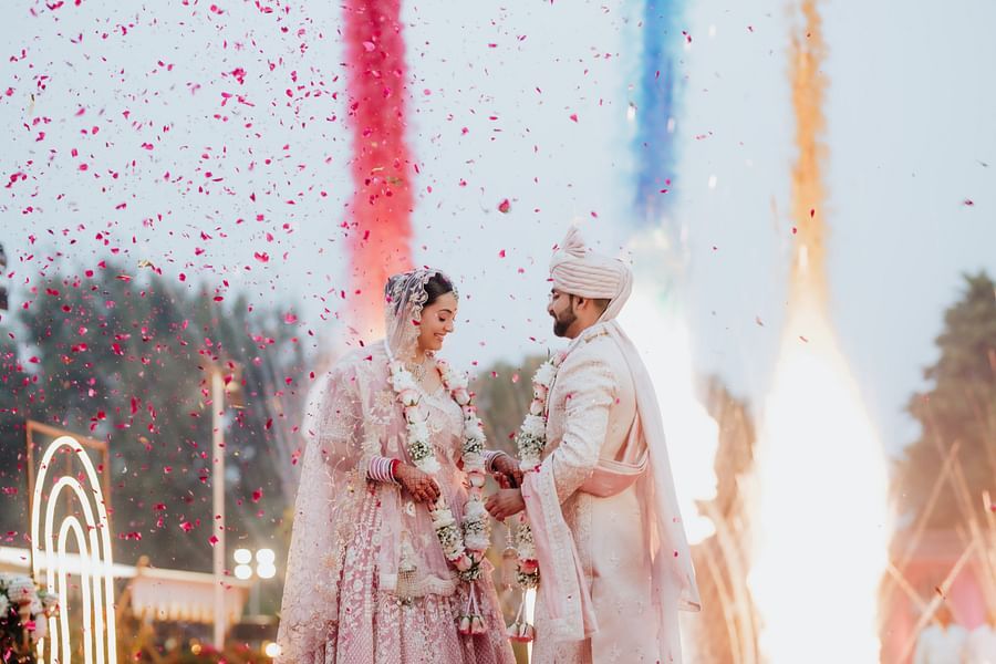 Bride and groom exchanging garlands under colorful smoke effects during the wedding ceremony.