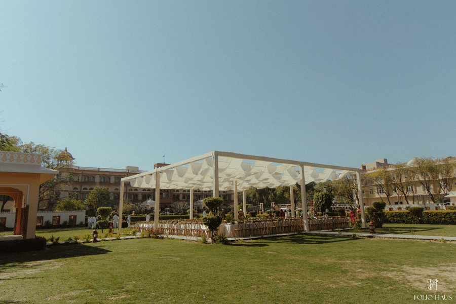 A wide view of a white wedding canopy tent set up on a large, manicured green lawn under a clear sky at Umaid Palace.