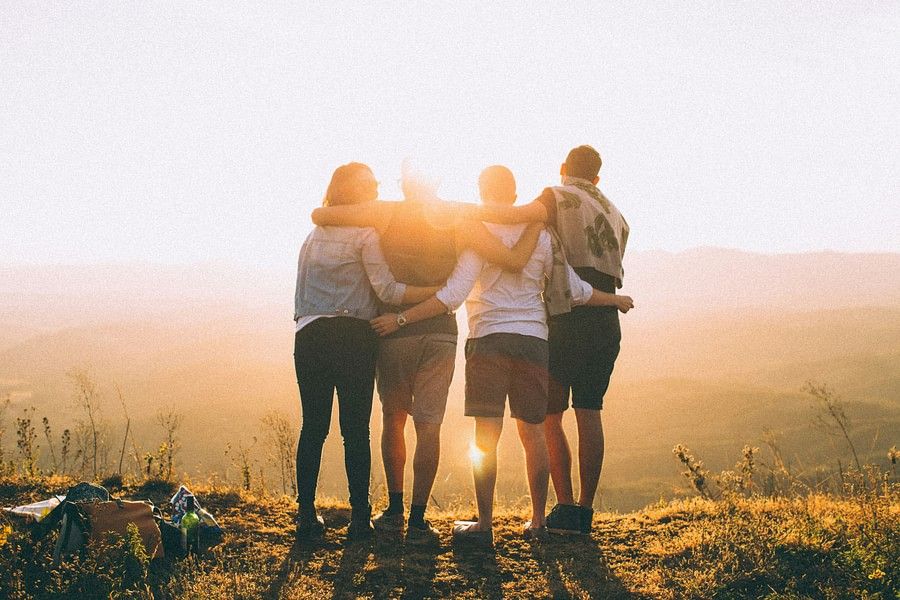 Four friends standing on a hill, silhouetted against a setting sun.