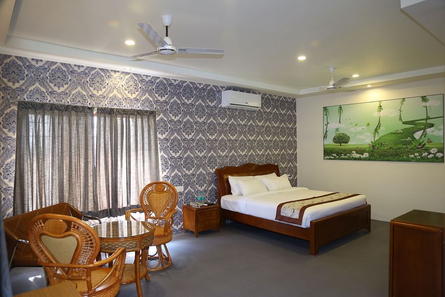 King size bed in the Themed Villa of GK Hill View Resort furnished with a wall-mounted AC, seating chairs for two, curtained windows.