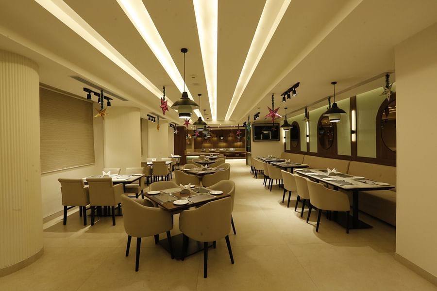  An image of a restaurant featuring several sets of tables, chairs, and sofa, lights hanging from the ceiling and mirrors attached on the wall at Tulip Inn, Zirakpur