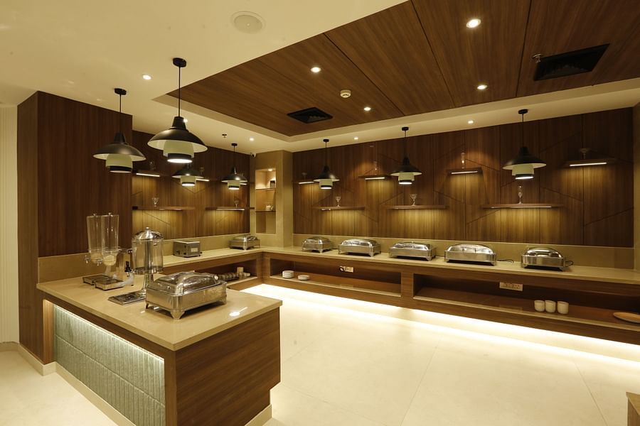 An image of a buffet hall featuring several covered utensils placed on the counter top and there are ceiling lights hanging from top - Tulip Inn, Zirakpur