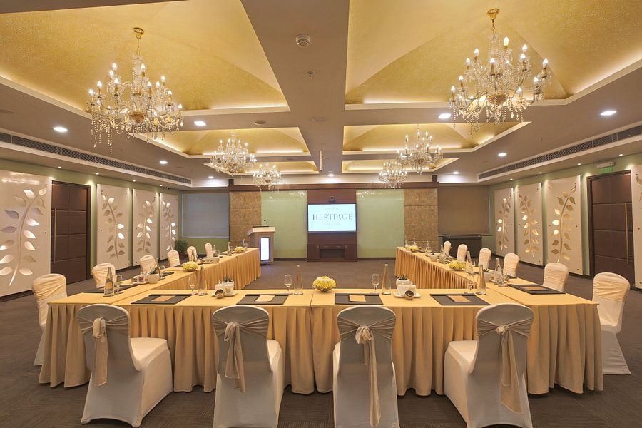 Well-lit conference room with a U-shaped table, elegant chandeliers, and a screen displaying HERITAGE - Heritage Village Resorts & Spa.