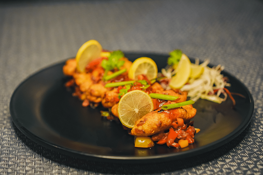 A plate of fried pakoda topped with veggies and sauce, accompanied by a side of salad and lemon