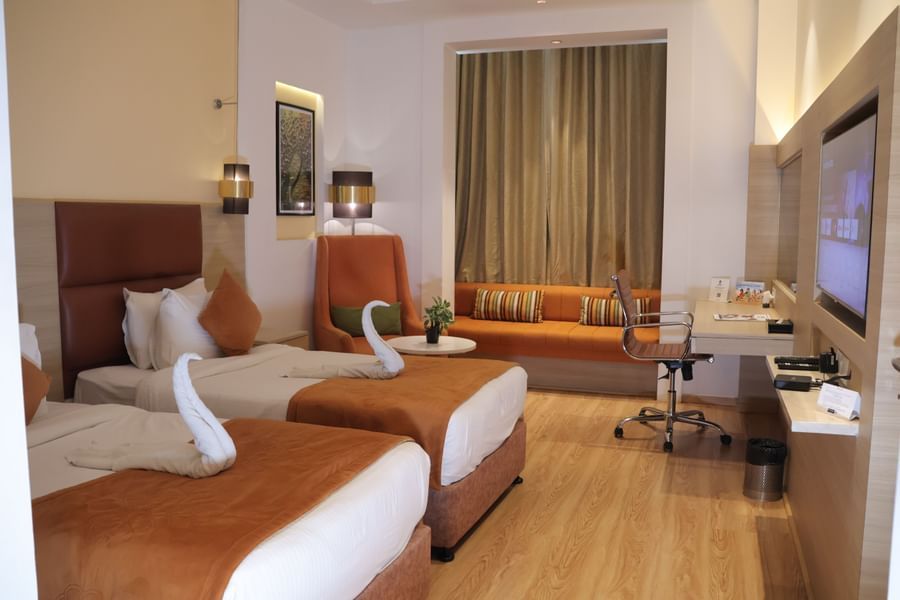 Twin bedroom with orange accent pillows, wooden furniture, seating chair and curtained window at Best Western, Vrindavan.