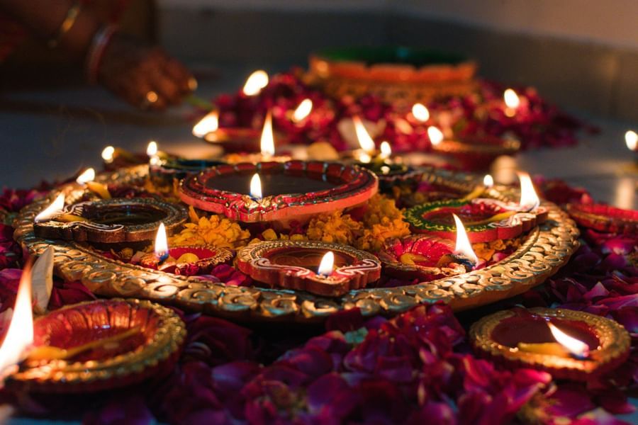 Small oil lamps lit during a hindu festival and the lamps are surrounded with flowers and loose petals.