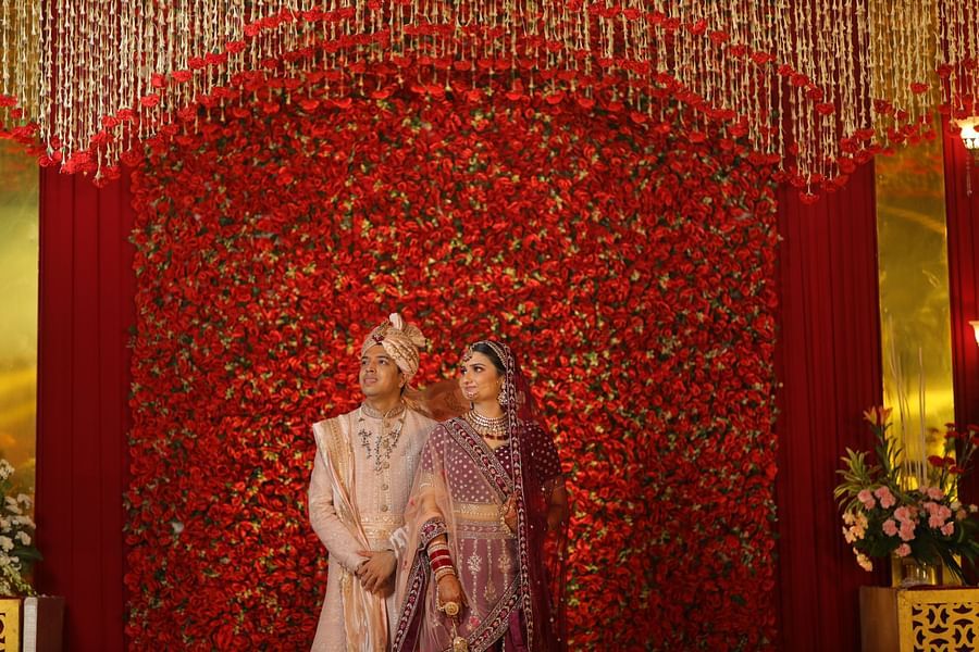 bride and groom posing for pictures with a backdrop of red - heritage village resorts & spa, Manesar