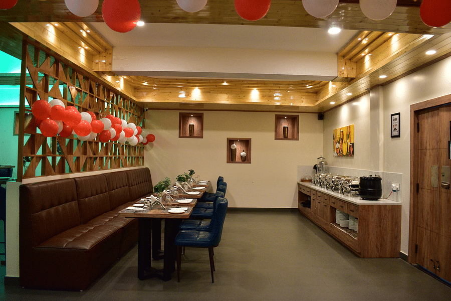 alt-text side angle view of dining table of a tea-seater dining table situated in front of the buffet area and decorated with red and white balloons - Hotel Montana Vyoo