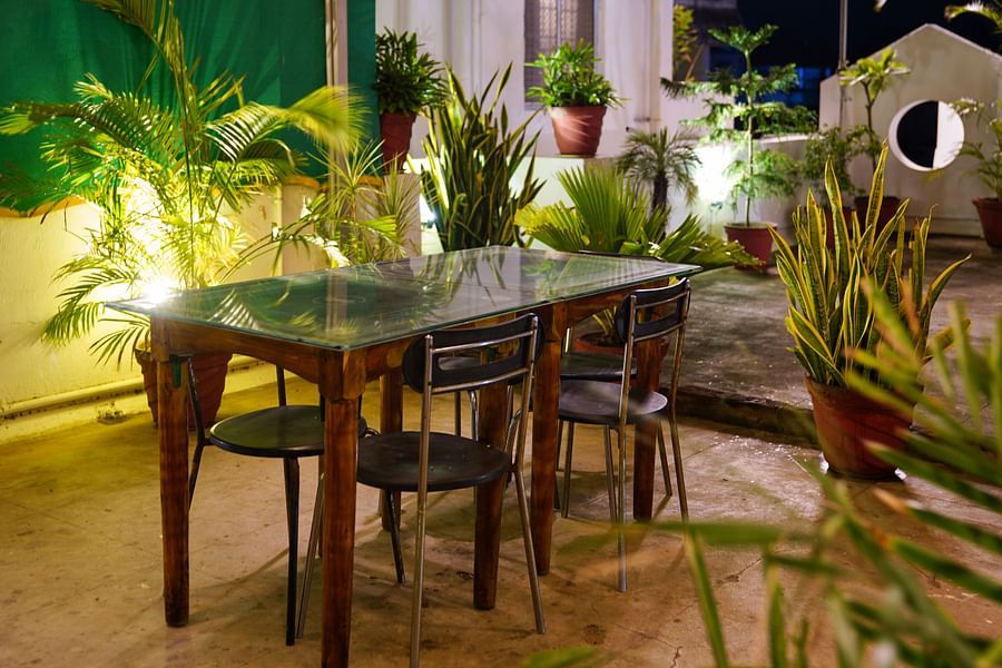 alt-text A rectangular table and chairs placed in an area surrounded by plants | La Paradise Residency, Pondicherry