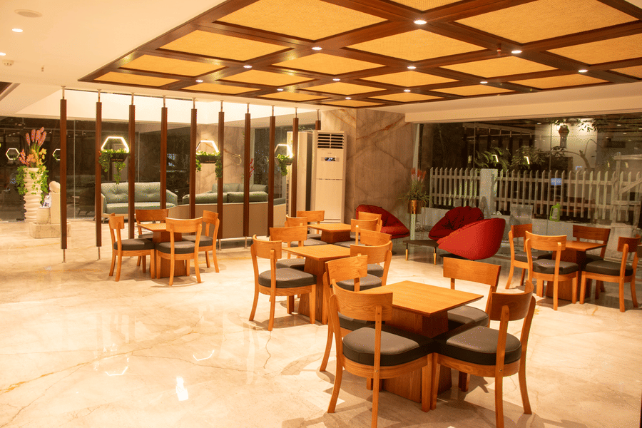 A hotel lobby area space with arranged tables and chairs, large windows, and patterned ceiling panels with lighting.