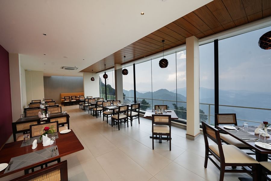 Chairs and tables in a restaurant with glass windows and mountain views | Misty Queen by Dimora, Kakkadampoyil