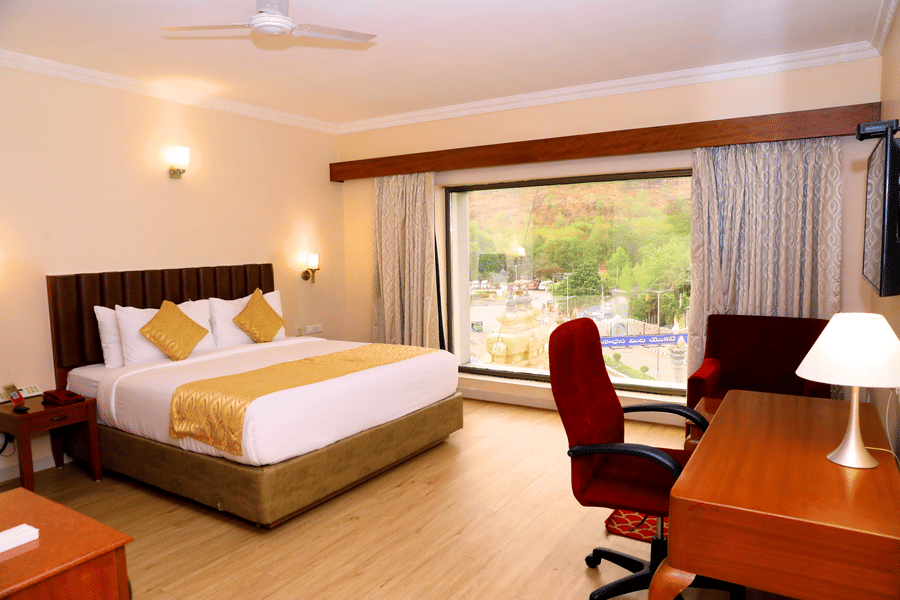 Hill View Room featuring a floor to ceiling window, a double bed, and desk and a chair inside Raj Park, one of the top hotels in Tirupati