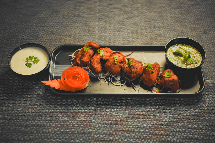 A chicken kebab on a rectangular plate, with sauce on the side and a small bowl of sauce beside it