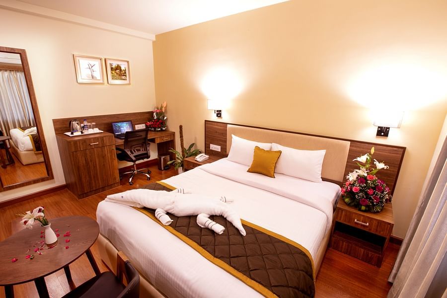 A warm and inviting hotel room with a plush bed, wooden furnishings, a work desk, and soft lighting for a cosy ambiance. - RK Gardenia, Surya City