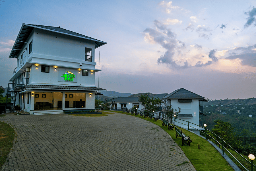 An exterior view of a white hotel building and grounds at twilight with a paved driveway and rolling hills in the distance | Abad Silvermist, Vagamon
