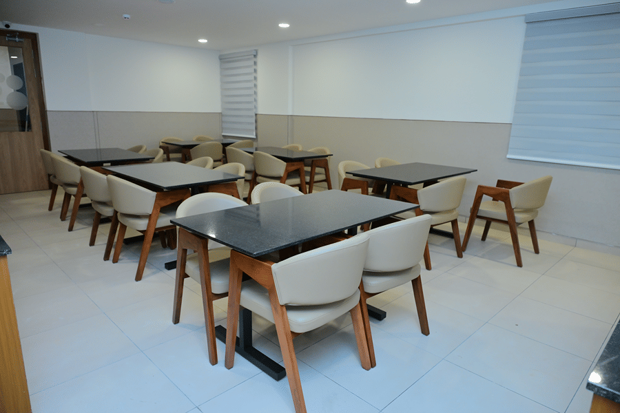 Modern restaurant interior at Bhavanis Vista By Icon Hosur with wooden dining chairs, dark-topped tables, and neutral-toned walls.