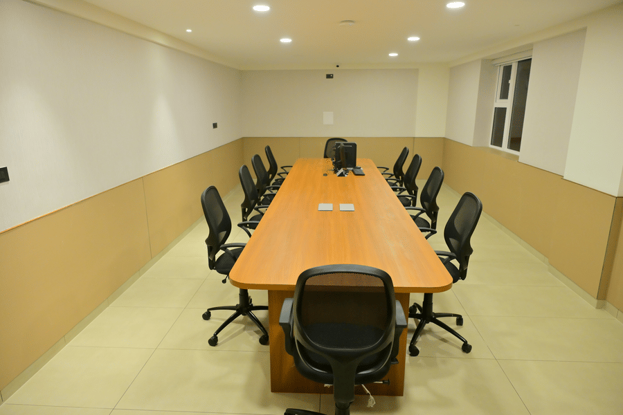 Bright meeting room at Bhavanis Vista By Icon Hosur with a long wooden table, black chairs, and recessed ceiling lights.
