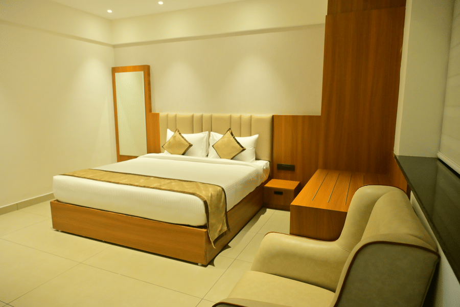 Suite bedroom at Bhavanis Vista By Icon Hosur with a king bed, wooden headboard panel, and a sofa seating area.