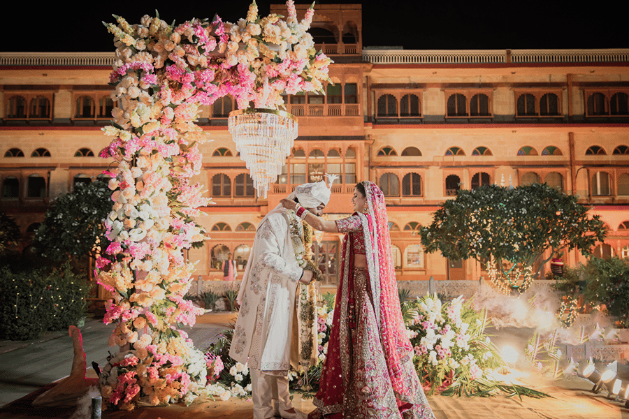 A couple in their wedding attire standing at the wedding alter with Umaid Palace, a royal wedding palace venue as their background.
