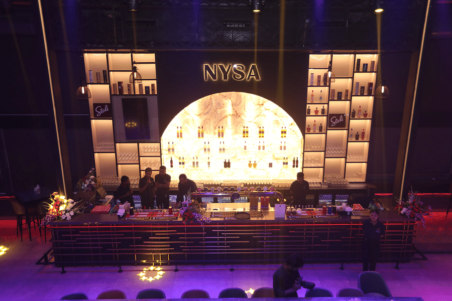 alt-text Stylish bar with illuminated shelves, a sleek counter, and staff preparing drinks in a vibrant setting - Nysa Skybar, Bengaluru