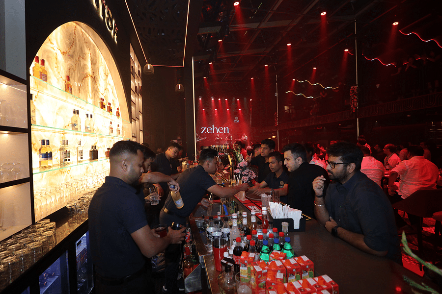 alt-text Energetic bar scene with attentive bartenders serving drinks against a vibrant backdrop, illuminated by red lights, creating a lively atmosphere for guests - Nysa Skybar