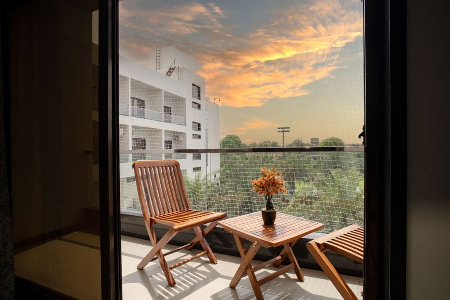 Hotel room balcony with wooden chairs and a table overlooking the surrounding area at sunset at Arawali Ananta Elite, Jaipur.