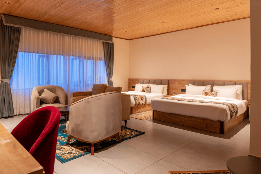 View of a room at Mount Hotel with a king bed, sofa seating, wooden ceiling, large windows, and warm ambient lighting.