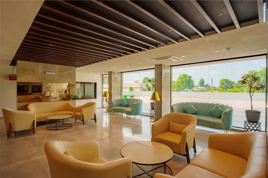 Another view of the lobby seating area featuring yellow armchairs and large windows overlooking the exterior at Arawali Ananta Elite, Jaipur.