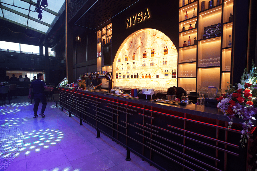 alt-text A vibrant bar showcasing a display of alcohol on shelves, set in a lively atmosphere with bartenders preparing drinks at Nysa Skybar, Bengaluru.
