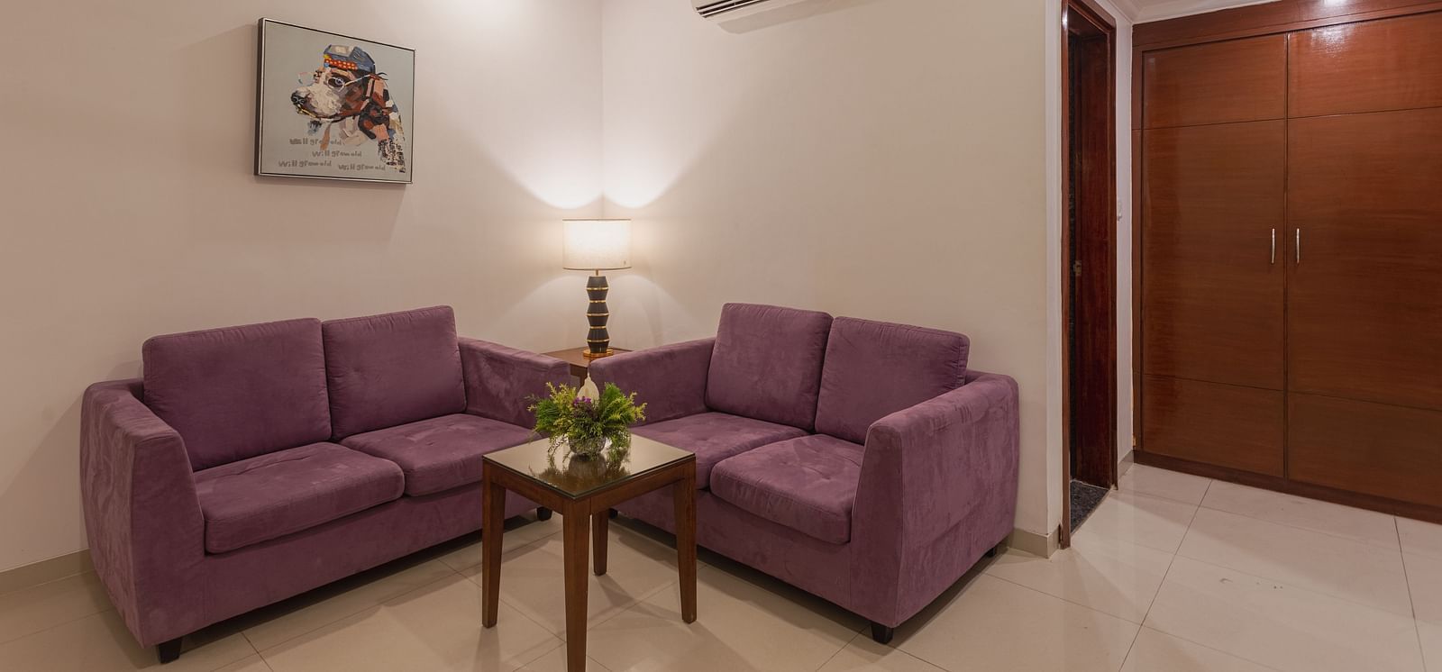An image of a living area in a suite at Diamond Palace Lords Plaza with two purple sofas and a small center table.