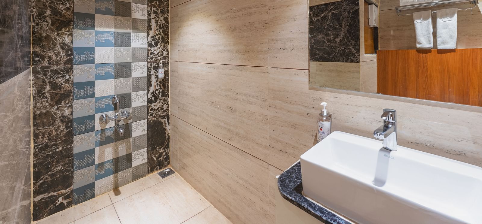 A modern bathroom features a rectangular sink, a shower area with patterned tiles, and a mirror reflecting the space - Lords Eco Inn Ambaji.